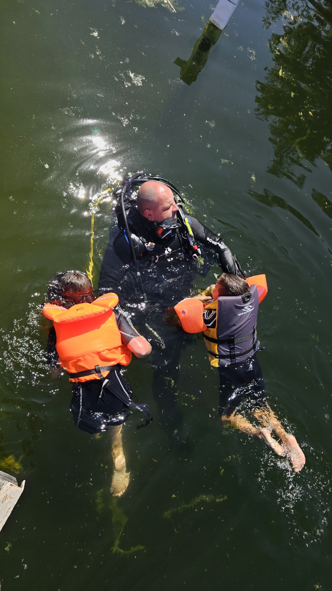 Instructor scafandru care sprijină doi copii cu veste de salvare în apa unui lac