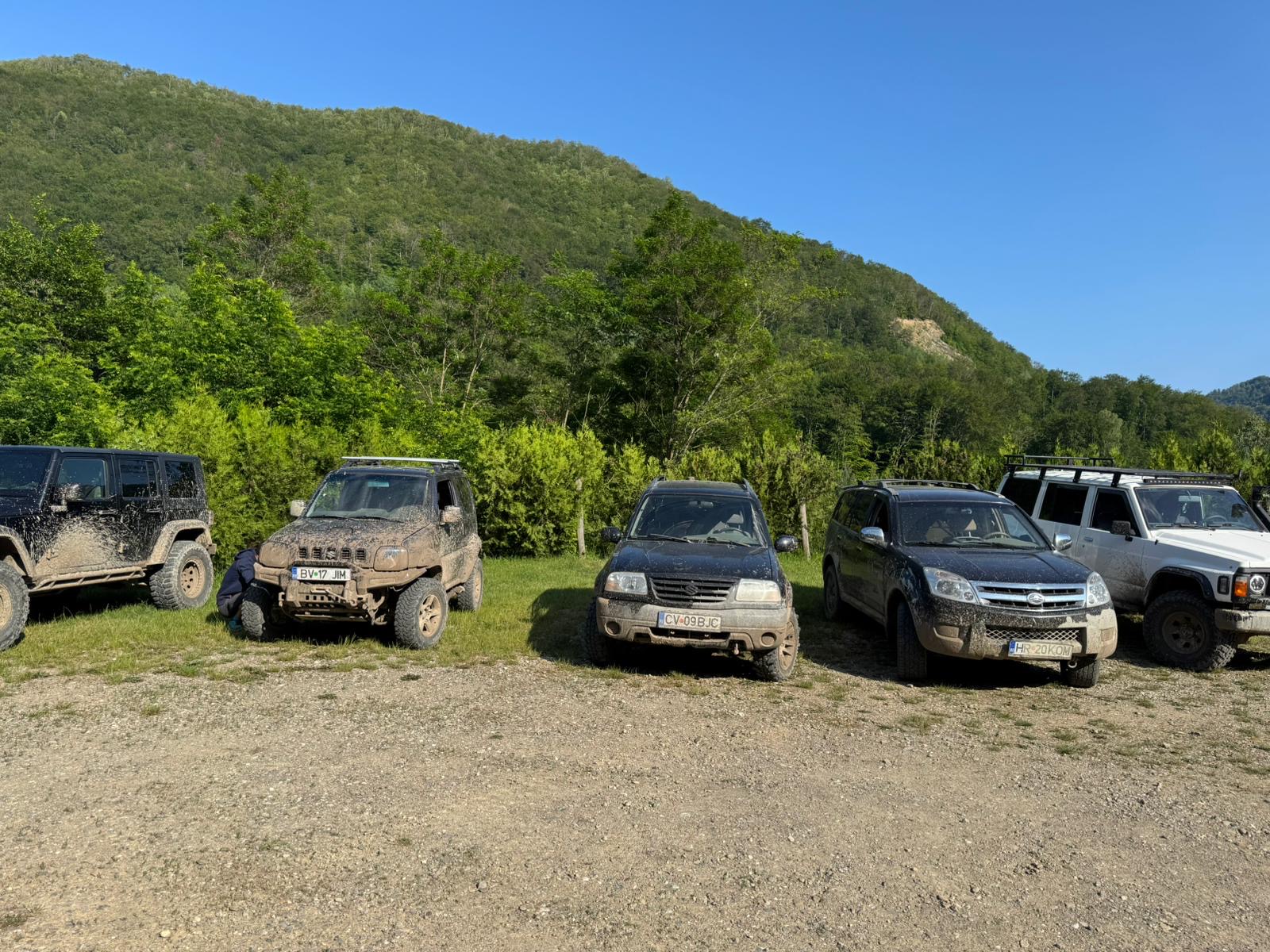 Mașini de teren pline de noroi, parcate la marginea pădurii înainte de o experiență